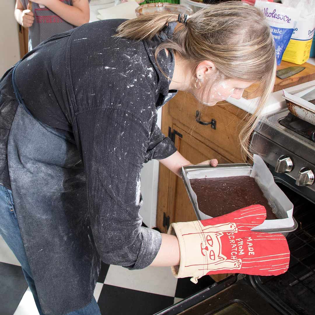 Woman with oven mitt putting a chocolate cake into the oven